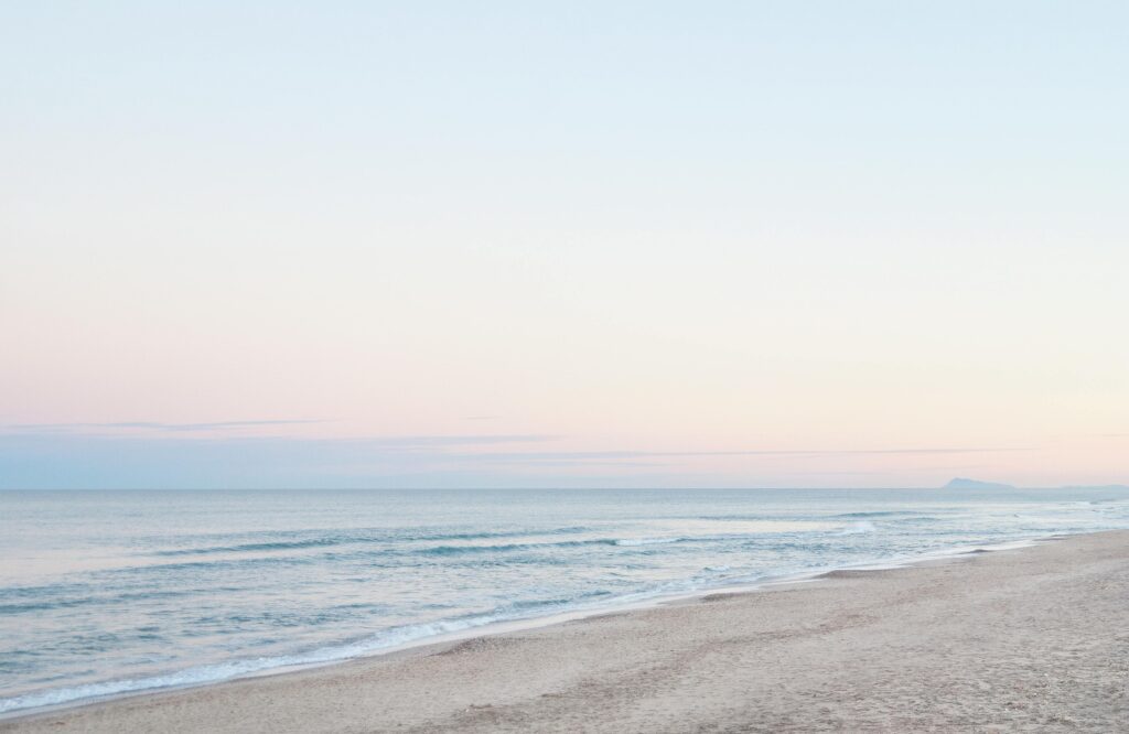 Calm coastal scene with gentle waves and pastel skies at dawn, offering tranquility.